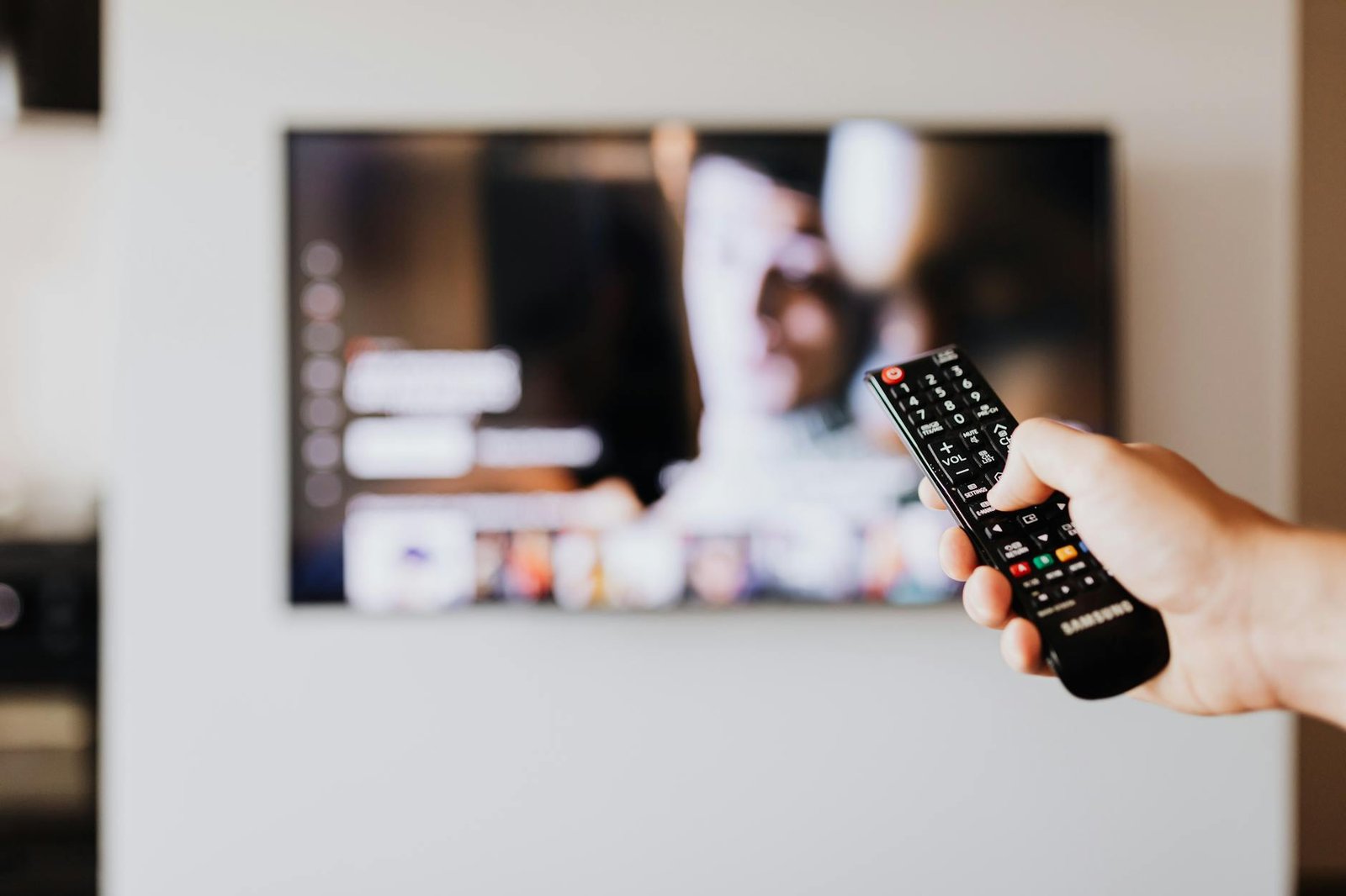 IPTV Channels Guide 2026 — Person aiming a TV remote with the channel grid blurred in the background | OTT-TV