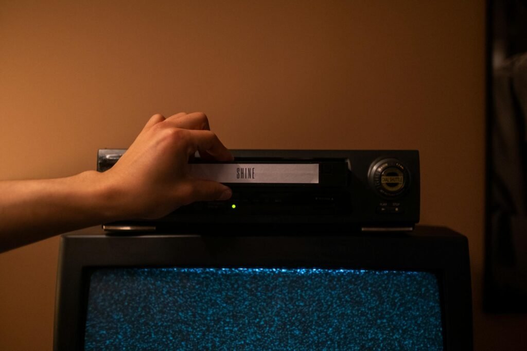 IPTV with Catchup — Hand inserting a tape into a video recorder above a TV displaying static, evoking playback and replay | OTT-TV