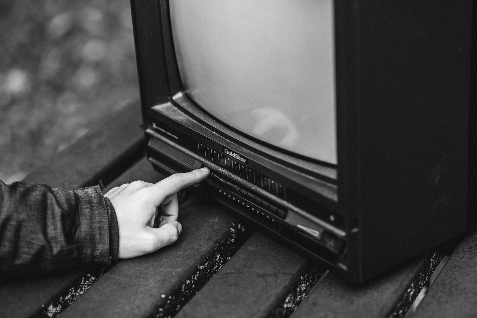 Black-and-white photograph of a vintage GoldStar CRT television with a hand pressing a physical channel button — the cable era ended, IPTV runs $10 to $17 a month versus cable's $83 average