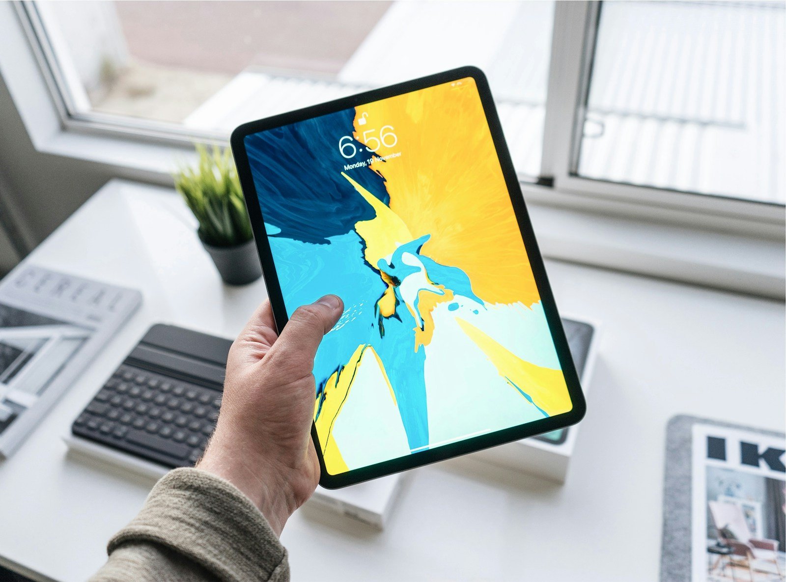 Hand holding an 11-inch iPad Pro at a desk, time on the lock screen — the iPad sits next to Firestick and Apple TV 4K as the most flexible IPTV streaming devices in 2026