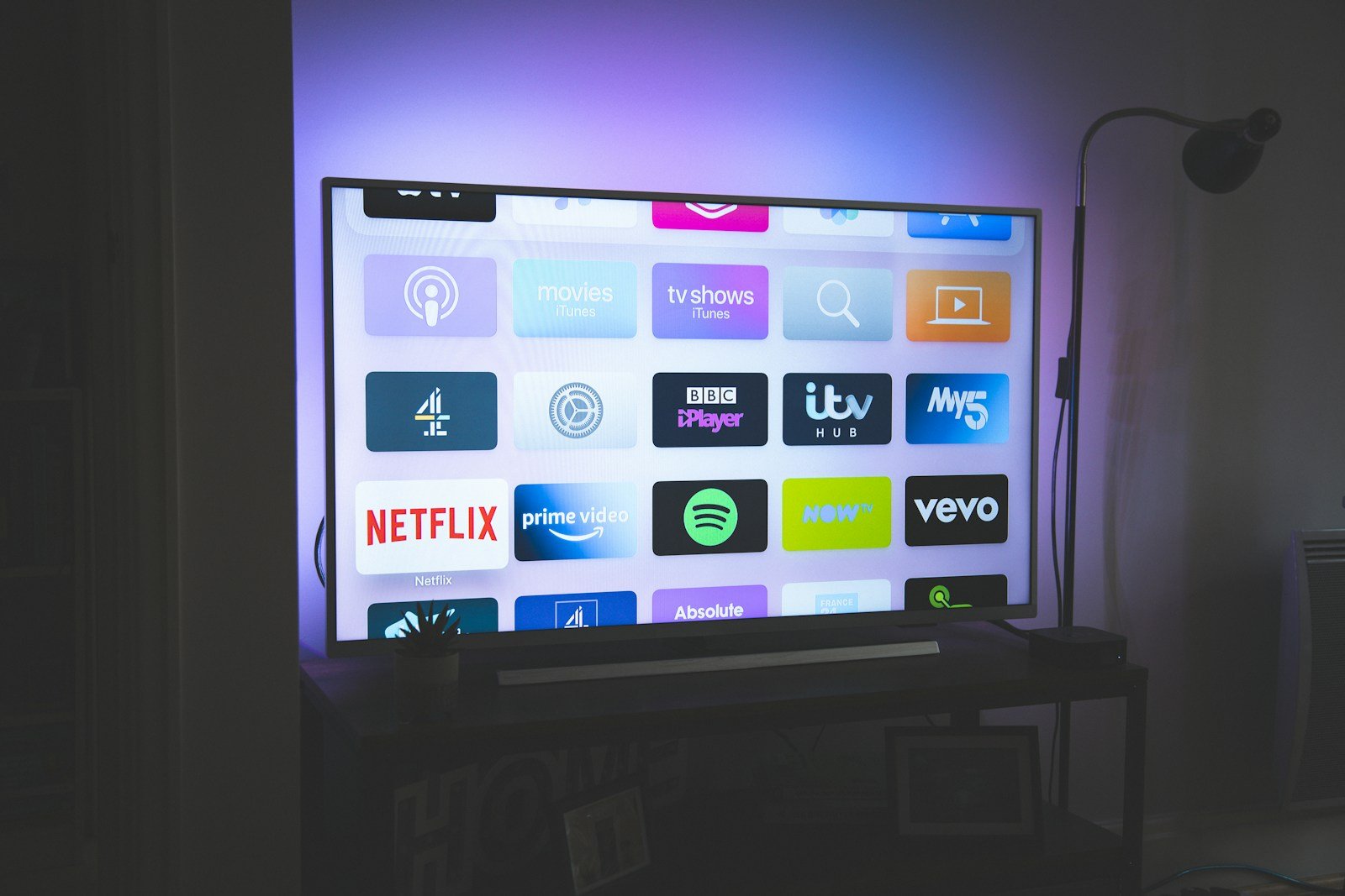Large Smart TV in a dark living room with ambient backlight glow, app grid showing Netflix, Prime Video, Spotify and movie tiles — five IPTV providers actually delivered after 183 days of testing